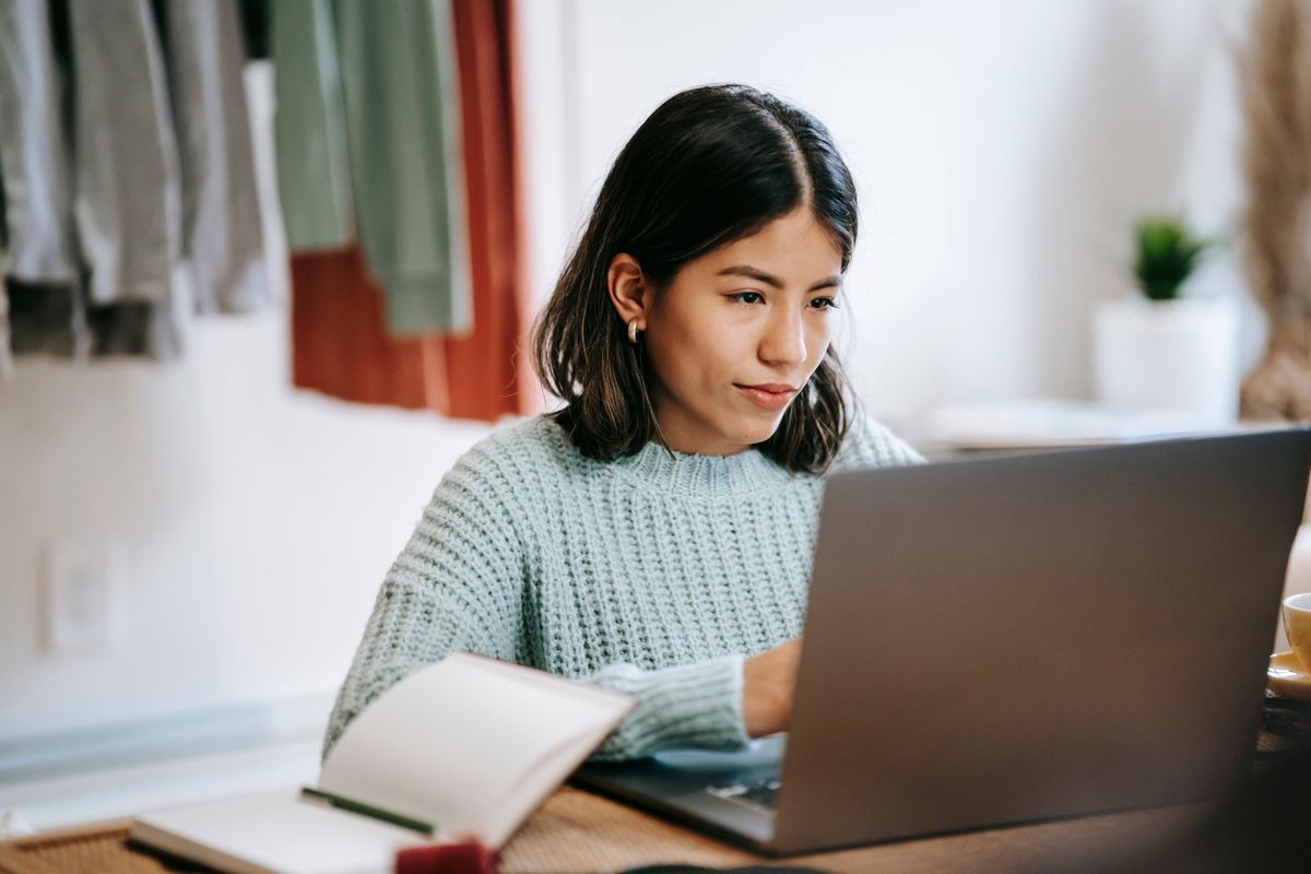 Mujer trabajando en una computadora portátil junto a un cuaderno.